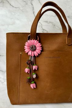 a brown leather bag with pink flowers on the front and side, sitting on a marble surface