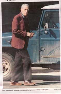 an old man standing in front of a blue truck looking at his cell phone while wearing slippers