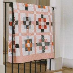 a pink and grey quilt hanging on a rail in front of a stair case with black iron handrails