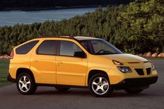 a yellow car parked on the side of a road next to some grass and trees