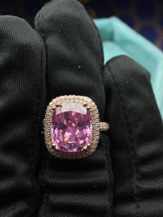 a fancy ring with a large pink stone surrounded by smaller round diamonds on black gloves