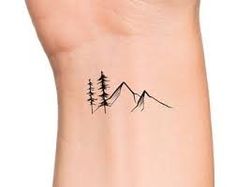 a small tattoo on the wrist of a woman with trees and mountains in the background