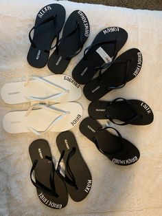 six pairs of flip flops are laid out on a white blanket with the names of each pair