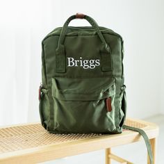 a green bag sitting on top of a wooden table next to a white wall with the words brigs written on it