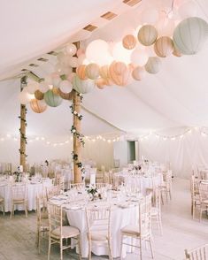 a room filled with lots of tables covered in white linens and paper lanterns hanging from the ceiling