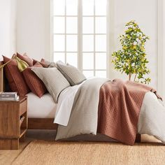 a bed with pillows and blankets on top of it next to a plant in a vase