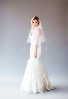 a woman in a white wedding dress and veil posing for the camera with her hands on her hips