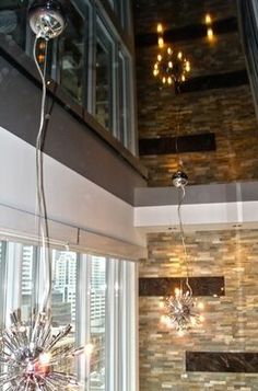 a chandelier hanging from the ceiling in a room with large windows and stone walls