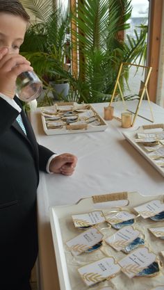 a young boy in a suit drinking from a glass next to some cookies on a table