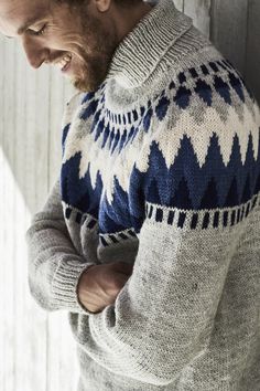 a man wearing a blue and white sweater standing in front of a wooden wall with his hands on his hips