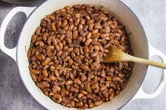 a pot filled with cooked beans on top of a table next to a wooden spoon