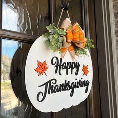 a happy thanksgiving sign hanging on the front door with pumpkins and leaves around it