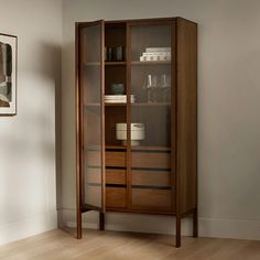 a tall wooden cabinet with glass doors in a room next to a painting on the wall