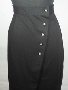 Here is a sweet vintage black knit midi skirt with a southern preppy, 1980's does 1940's style. This classic and collectible Fritzi, made in U.S.A. label, cotton polyester knit midi skirt has really great tailoring details from a tailored high waistband to the down-the-front button closure design. This cute wrap over cut knit skirt has chic style with its sleek straight cut and the vintage label says it's a **vintage size** 10 and since it's a vintage size, flat measurements are here to check yo Elegant Black Pencil Skirt With Buttons, Black Pencil Skirt With Button Closure For Work, Fitted Knee-length Skirt With Side Buttons, Formal Knee-length Skirt With Buttons, Formal Black Skirt With Button Closure, Classic Pencil Skirt With Buttons, Black Buttoned Skirt For Formal Occasions, Formal Fitted Pencil Skirt With Button Closure, Black Skirt With Buttons For Formal Occasions