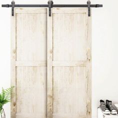 a pair of sliding doors in front of a potted plant and white wall with black metal handles