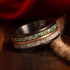 two wedding bands with green and white wood inlays are sitting on a wooden surface