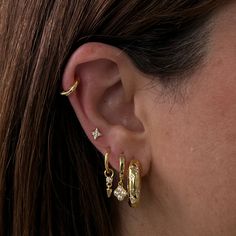 a close up of a woman's ear wearing gold earrings and diamond hoops