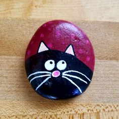 a painted rock with a black cat on it's face sitting on a wooden surface