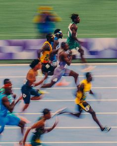 a group of men running on top of a blue track covered in yellow and green uniforms