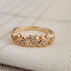 a gold ring with three hearts on it sitting on top of a white cloth next to a pillow