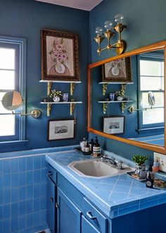 a bathroom with blue tile and gold fixtures on the wall, along with two framed pictures