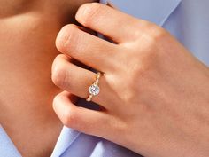 a woman's hand with a diamond ring on her left side, wearing a blue shirt