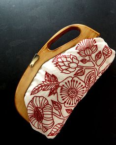 a handbag with red flowers on it sitting on top of a black table next to a pair of scissors