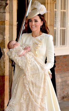 a woman holding a baby wearing a dress and hat