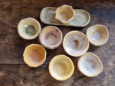 nine ceramic bowls with different shapes and sizes on a wooden surface, including one that has been turned upside down