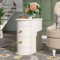 a white dresser with flowers and books on it in front of a stair case next to a chair