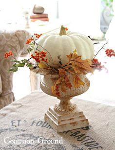 a white pumpkin sitting on top of a vase filled with autumn leaves and orange berries