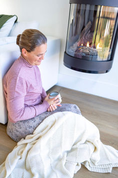 a woman sitting on the floor next to a fire place with a blanket over her