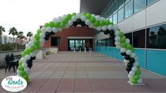 an arch made out of balloons in front of a building with tables and chairs around it