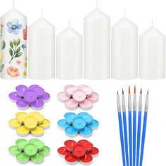 several different colored candles and paint brushes next to each other on a white background with flowers