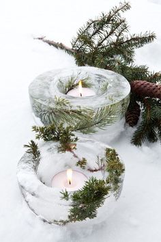 two candles are sitting in the snow next to some pine cones and evergreen branches,