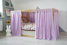 a child's bed with purple curtains and a white rabbit toy in the corner