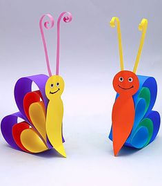 two colorful paper butterflies sitting on top of each other, one with a smiling face