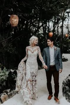 a bride and groom holding hands walking through the woods in their wedding attire with feathers on them