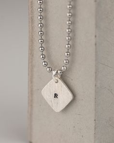 This army inspired necklace with hand stamped square silver tag makes a unique gift for a young man. We can stamp a maximum of 2 characters on the sterling tag, which hangs from a 50cm steel ball chain with barrel closure. The necklace is personalised to order in our studio on the Isle of Wight in England and is sent to you inside our stylish, grey gift box. - Sterling silver 925 tag - Hand stamped - Dog tag style steel ball chain - Eco-friendly gift box Size: 50cm steel chain (19.5"), 1.2cm squ Rectangular Tag Jewelry For Gifts, Hand Stamped Sterling Silver Rectangular Necklaces, Sterling Silver Jewelry With Box Chain And Dog Tag, Hand Stamped Rectangular Sterling Silver Necklaces, Hand Stamped Sterling Silver Rectangular Necklace, Classic Silver Dog Tag Necklace, Square Steel Tag Necklace, Everyday Stamped Dog Tag Necklace, Sterling Silver Dog Tag Necklace