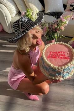 a woman kneeling down with a cake in front of her on the floor next to a couch