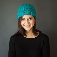 a woman wearing a green knitted hat smiling at the camera with her hands in her pockets