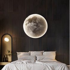 a bed with white sheets and pillows in front of a large moon on the wall