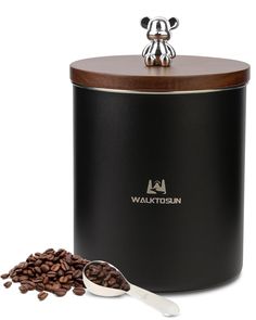 a black coffee canister with a spoon next to it and some beans on the ground