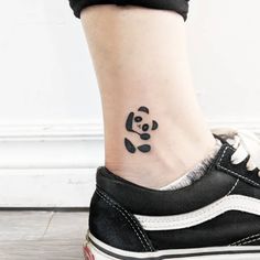 a small panda bear tattoo on the side of a woman's ankle, with black ink