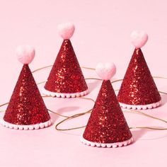 red glitter party hats with white pom poms on them, sitting on a pink background