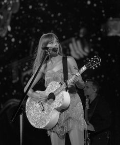 a woman holding a guitar and singing into a microphone