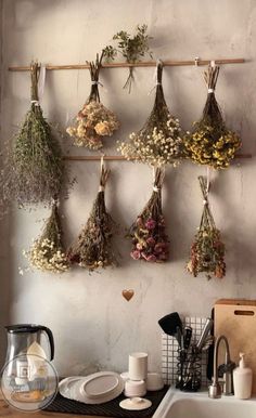 dried herbs hanging on the wall above a sink in a kitchen with a tea kettle and coffee pot