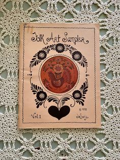 an old book is sitting on a lace doily with the title'folk art sampleer vol 1 '