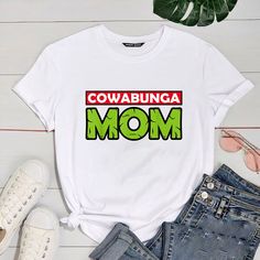 a t - shirt with the words cowabunga mom printed on it next to jeans and sunglasses