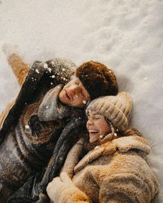 two people laying in the snow with their arms around each other and one person smiling